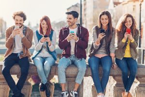 Eine Gruppe junger Leute sitzt mit ihren Smartphones auf einer Mauer in der Stadt